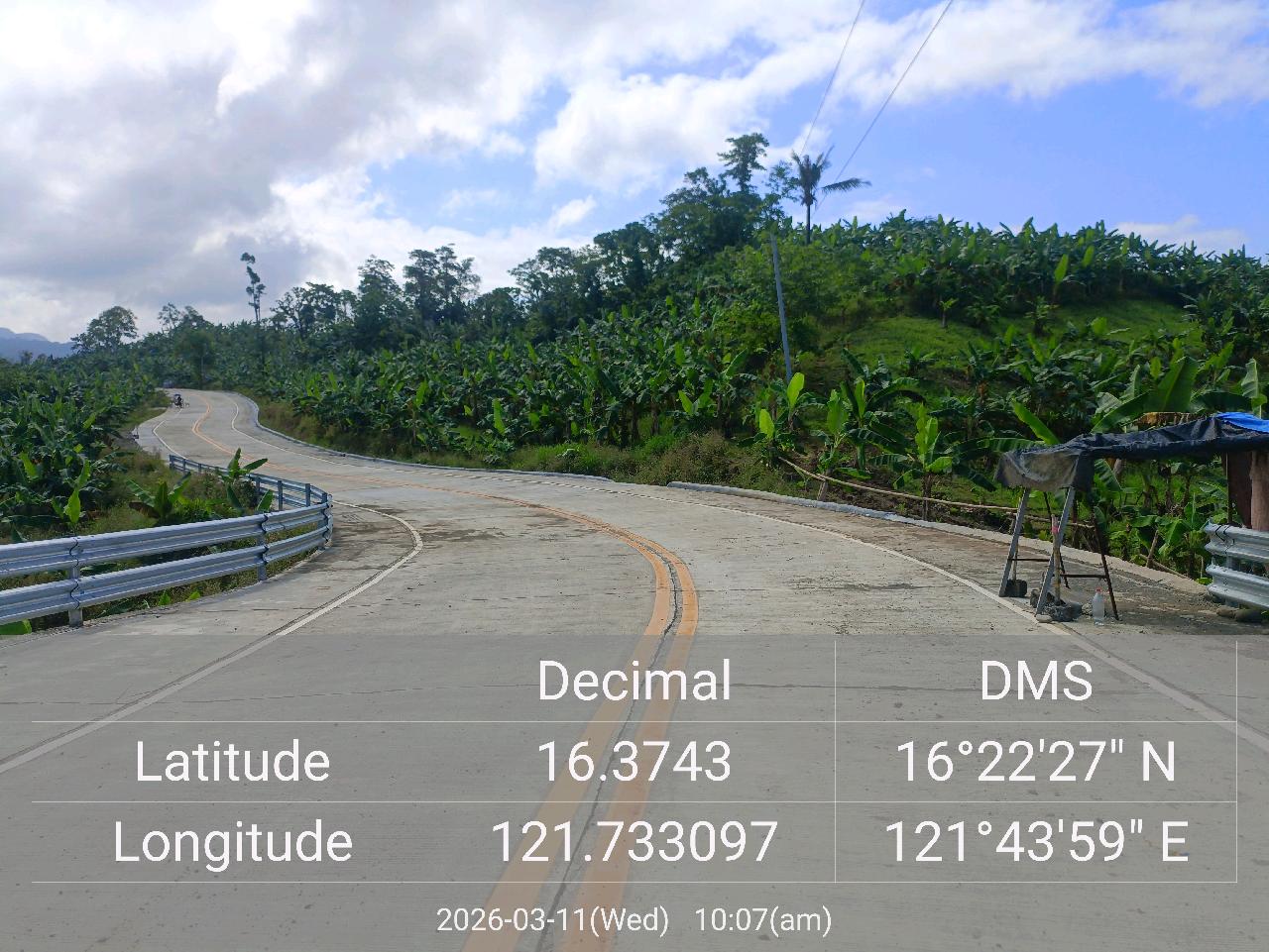 Completed concrete access road winding through farmland with guardrails